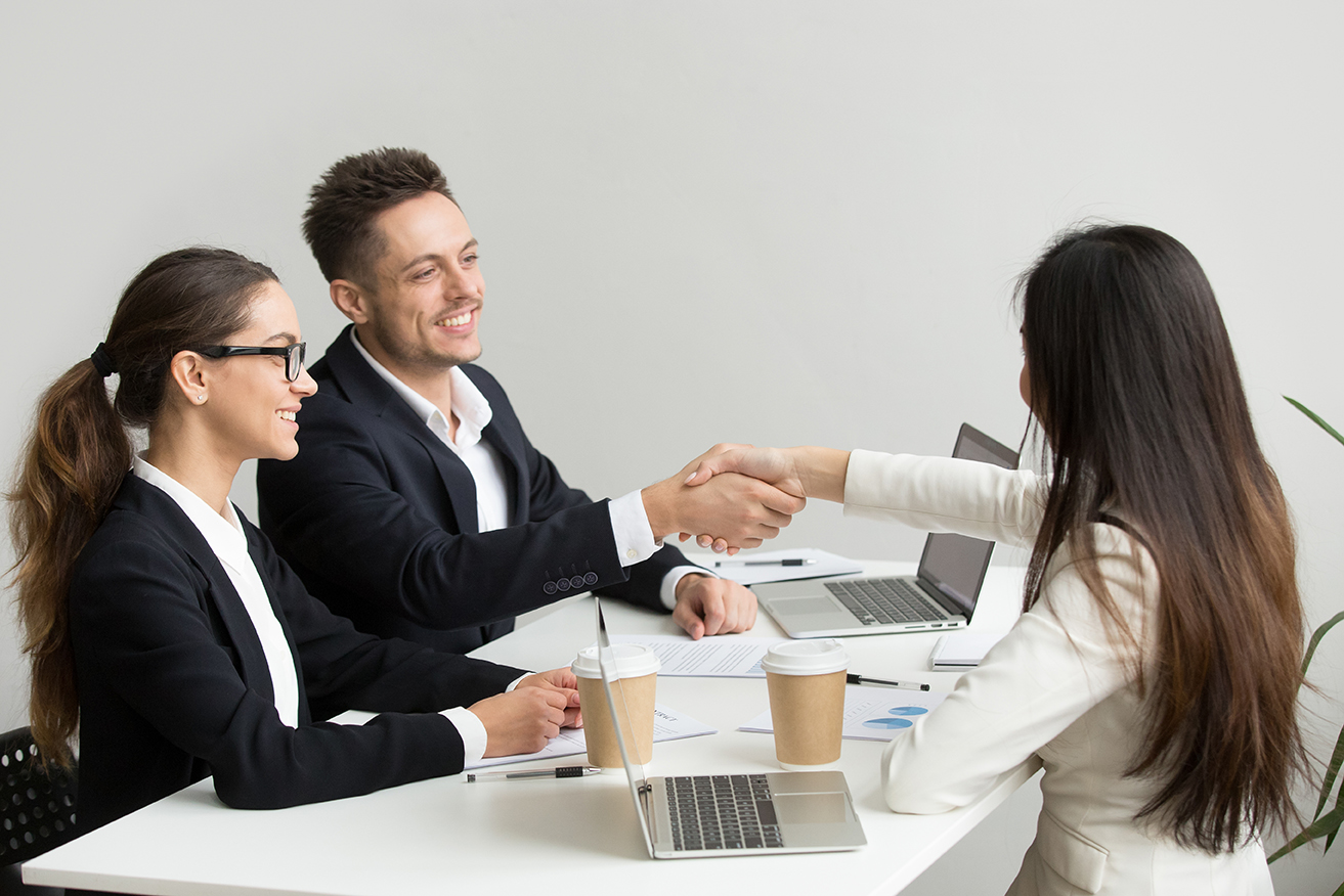 Friendly satisfied partners handshaking at group meeting thanking for successful teamwork, smiling millennial businessman shaking hand greeting businesswoman, respect or making contract deal concept